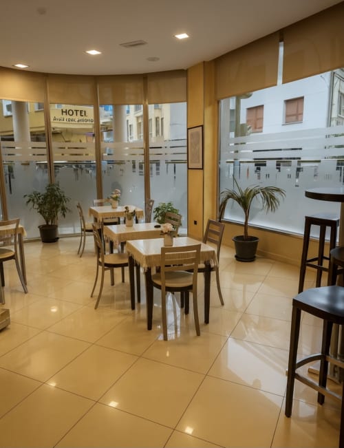 Sala de desayunos del Hotel Villa de Cacabelos con sillas de madera, mesas redondas, plantas en macetas y amplias ventanales con vistas al