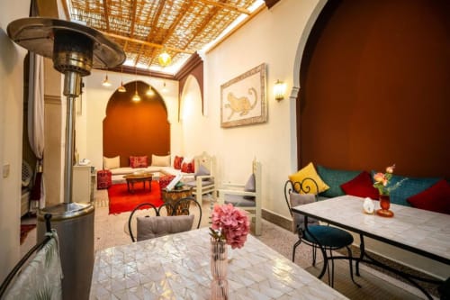 Chambre triple riad de Marrakech avec alcôve voûtée, coussins colorés, coin repas en patio et décor marocain traditionnel