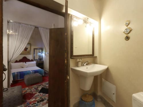 Salle de bains avec lavabo sur colonne et miroir dans la Chambre Quadruple de la Villa El Gada à Marrakech, vue vers la chambre