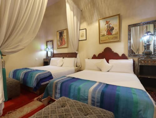 Chambre quadruple à la Villa El Gada de Marrakech avec deux lits, literie rayée bleue, rideaux crème et décor marocain traditionnel