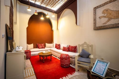 Chambre triple à Villa El Gada à Marrakech avec alcôve voûtée, accents rouges, sièges confortables et décor marocain traditionnel.