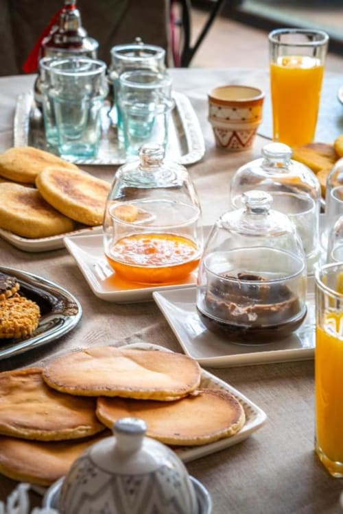 Table de petit-déjeuner à la Villa El Gada Marrakech avec viennoiseries, pains, jus, eau et confiture sous cloches