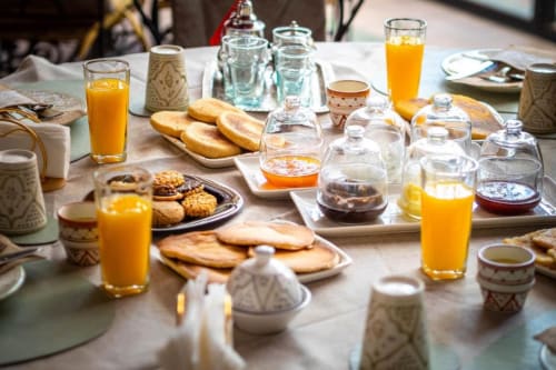 Table du petit-déjeuner à Villa El Gada avec jus d'orange, pain, pâtisseries et vaisselle marocaine traditionnelle à Marrakech