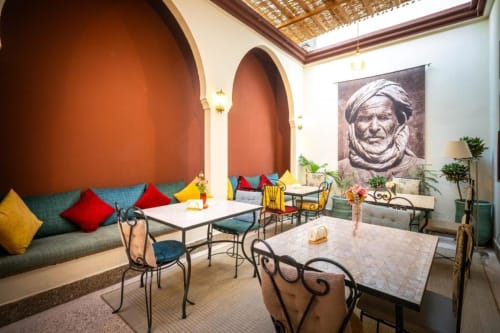 Chambre Triple Villa El Gada à Marrakech avec coussins colorés, arches traditionnelles et salle à manger aux murs en terre cuite