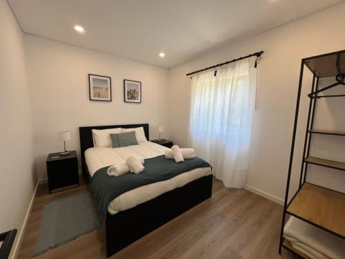 Quarto moderno da villa Casa do Sol Norte em Gemeses com cama preta, roupa de cama branca, vista para jardim e piso em madeira