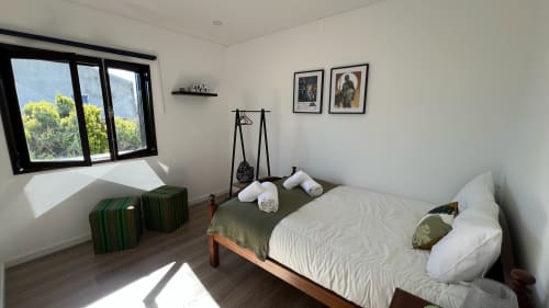 Quarto luminoso na villa Casa do Sol Norte com cama de madeira, roupas de cama brancas, vista do jardim pela janela, quadros emoldurados e verde