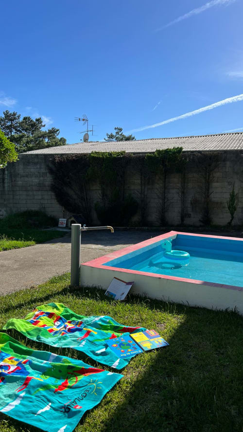Pipas coloridas dispostas na grama ao lado da piscina turquesa vazia da villa Casa do Sol Norte em Gemeses, Portugal
