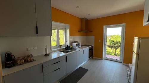 Cozinha moderna com armários brancos, paredes laranja e vista para o jardim da Casa do Sol Norte, Gemeses