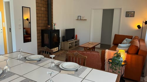 Sala de jantar e estar da villa Casa do Sol Norte com lareira, TV, sofá laranja e vistas para o jardim em Gemeses, Portugal