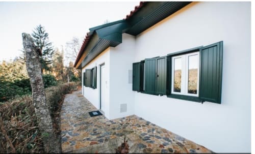 Terraço da vila Casa Lobos com caminho de pedra, paredes brancas, portadas verde-escuro e vistas do jardim em Vieira do Minho