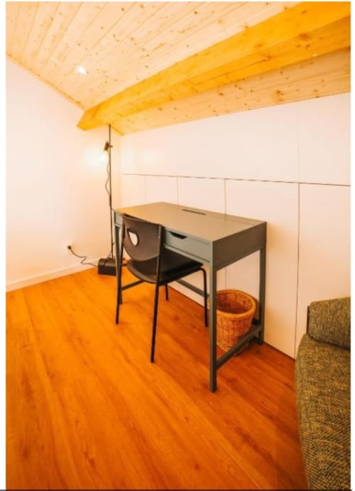 Espaço de trabalho em loft moderno na villa Casa Lobos em Vieira do Minho com vigas de madeira, escrivaninha, cadeira, piso laranja e vistas para o jardim