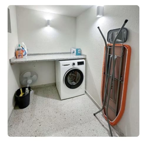 Moderna lavanderia da villa Casa Lobos com máquina de lavar branca, bancada cinza e armário organizado para produtos de limpeza.