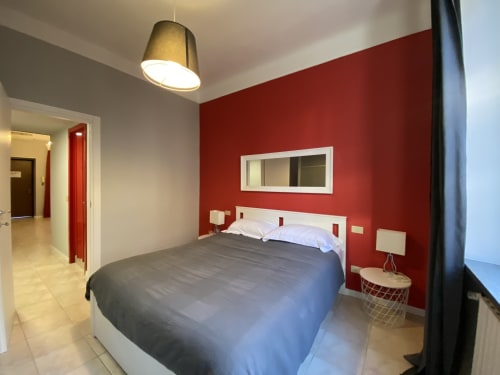 Camera da letto moderna a Milano con parete rossa, letto matrimoniale, lampada a sospensione e vista città—Urban ESCAPE G 230