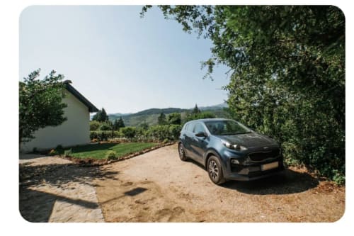 SUV azul escuro estacionado na entrada de cascalho da villa Casa Colina em Salamonde, Portugal, com edifício branco e vistas para a montanha