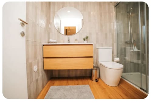Banheiro moderno na villa Casa Colina com gabinete em madeira, espelho redondo, vaso sanitário e box de vidro na Remote Care & Co