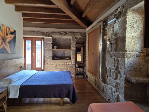 Dormitorio rústico de piedra en Aldea Rural Pazos de Arenteiro con vigas de madera, chimenea y paredes vistas en Pazos de Arenteiro