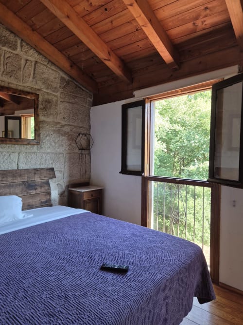 Dormitorio rústico con vigas de madera vista, muros de piedra y vistas a árboles verdes en Aldea Rural Pazos De Arenteiro