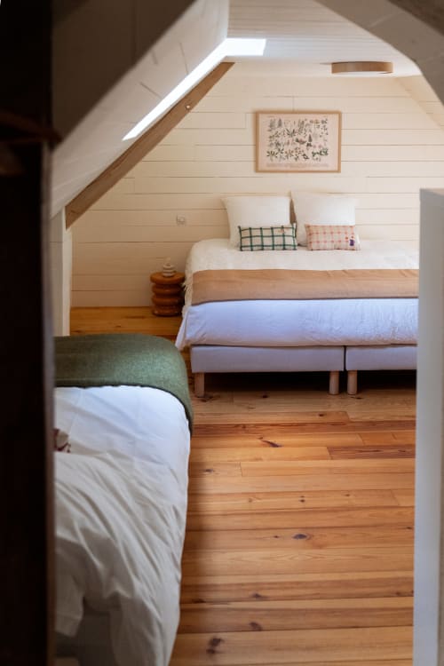 Chambre lumineuse sous les combles à la BnB Maisons Noisette avec lits en bois, murs blancs, puits de lumière et parquet rustique.
