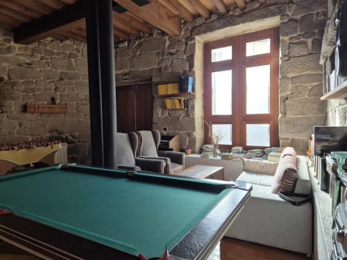 Rústica sala de juegos de piedra con mesa de billar en Aldea Rural Pazos de Arenteiro, con vigas vistas y puertas rojas
