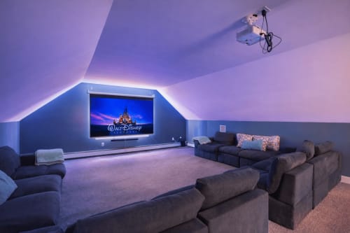 Modern home theater in Malkita Aria villa, Woodbury. Dark seating, purple ambient lighting, wall-mounted screen.