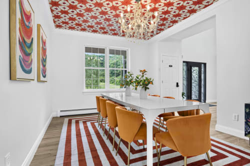 Modern kitchen and dining area in Malkita Aria villa with orange chairs, white island, red patterned ceiling, and mountain