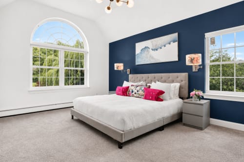 Modern bedroom in Malkita Aria villa, Woodbury, with gray upholstered bed, navy accent wall, mountain views through large