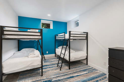 Modern bedroom at Malkita Homes villa in Woodbury with two black bunk beds, white bedding, and vibrant teal accent wall.