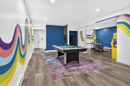Colorful recreation room at Malkita Aria villa in Woodbury featuring pool table, wavy rainbow wall art, and blue accent