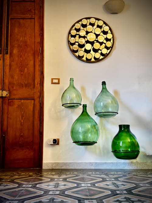 Ingresso dell'appartamento a Lecce con porta in legno, bottiglie decorative di vetro verde e arte murale circolare con candele