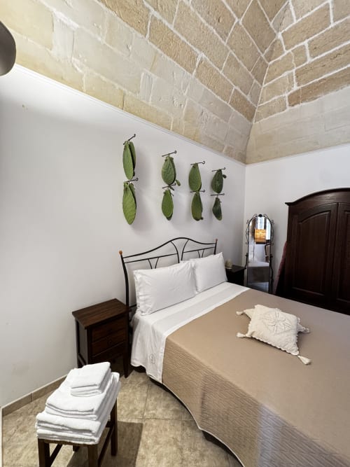 Camera da letto accogliente in appartamento a Lecce con letto in ferro battuto, biancheria bianca, mobili in legno scuro e decorative foglie verdi a parete