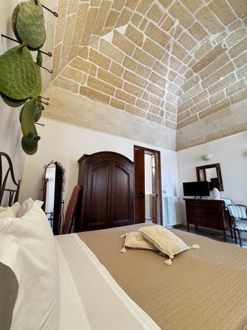 Ampia camera da letto nell'appartamento HABITARE Lecce con soffitto in mattoni a vista, armadio in legno scuro e vista sulla città di Lecce, Italia