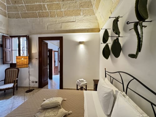 Camera luminosa nell'appartamento HABITARE Lecce con muri bianchi, letto in ferro battuto, arte botanica a muro e mattoni a vista