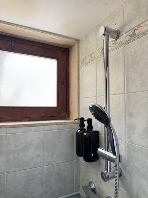 Area doccia del bagno dell'appartamento HABITARE Lecce con pareti piastrellate, soffione cromato e accessori neri