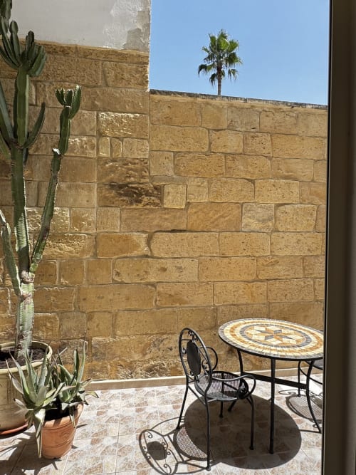 Terrazza di HABITARE Lecce con muri in pietra, tavolo con mosaico, cactus e vista palme nel Salento