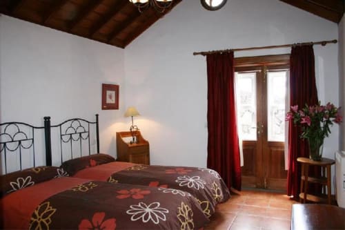 Dormitorio amplio en villa La Caldera Country House con cama de hierro forjado, pisos de terracota, cortinas burdeos y vistas al océano