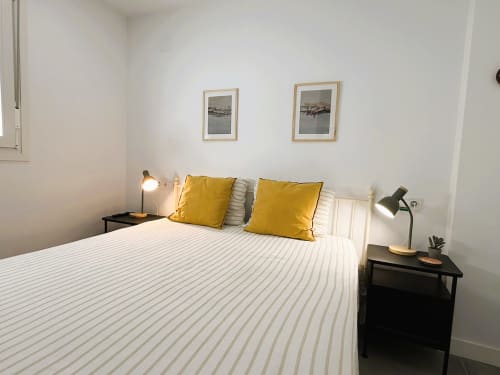 Dormitorio moderno en apartamento frente al mar en Fuengirola con ropa de cama blanca a rayas, almohadas amarillas y mesitas de noche negras