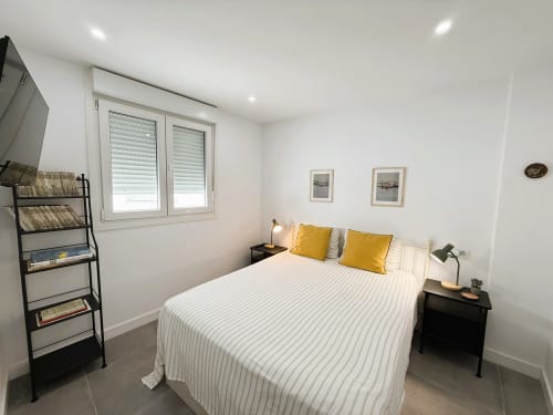 Dormitorio moderno en apartamento de lujo frente al mar en Fuengirola con ropa de cama rayada, almohadas amarillas y decoración minimalista