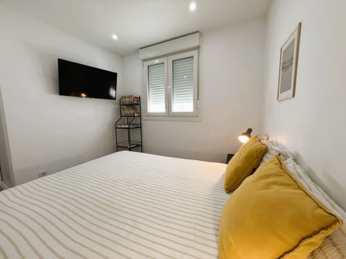 Dormitorio moderno en apartamento de lujo frente al mar, Fuengirola, con cama a rayas, almohadas amarillas, TV de pared y ventana con
