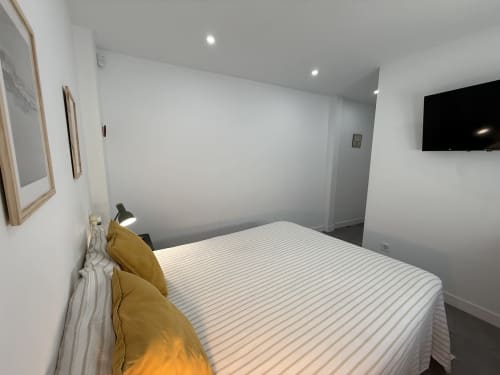 Dormitorio moderno con almohadas amarillas, ropa de cama a rayas y TV de pared en lujoso apartamento frente al mar, Fuengirola