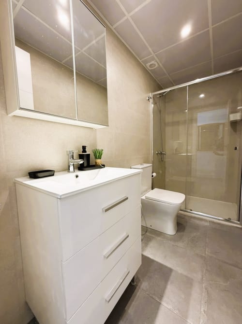 Baño moderno en apartamento de lujo frente al mar en Fuengirola con vanidad blanca, inodoro y ducha con mampara de cristal