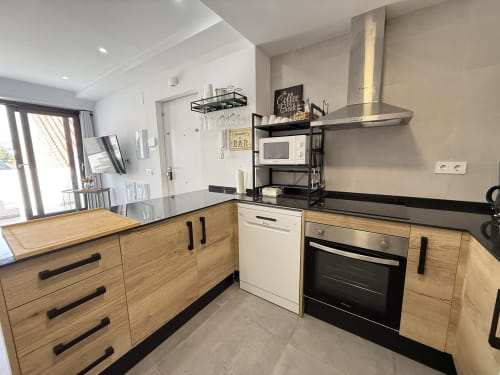 Cocina moderna con muebles de madera, electrodomésticos de acero inoxidable, encimeras negras y barra de desayuno en lujosa Fuengirola