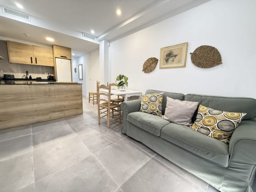 Sala de estar y cocina modernas en lujoso apartamento frente al mar en Fuengirola con sofá gris, sillas de comedor de madera y tejidos artesanales
