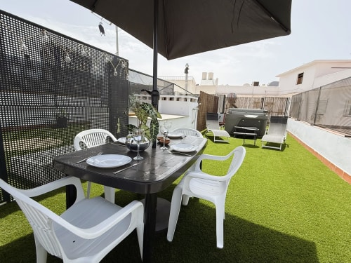 Terraza de lujo con vistas al mar en Fuengirola: mesa de comedor, sillas blancas, sombrilla negra, césped artificial