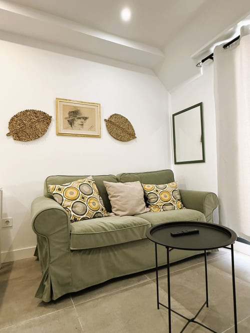 Sala de lujo en Fuengirola con sofá verde salvia, decoración tejida en pared y mesita negra moderna