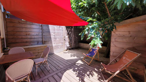Terrazza privata del Lodge du Cap Ferret con ombrellone rosso, pavimentazione in legno, lettini e vista sul lussureggiante giardino