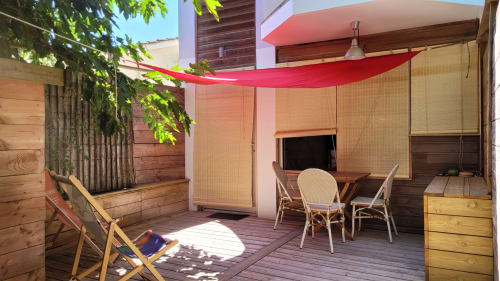 Terrazza privata soleggiata presso Le Lodge du Cap Ferret con vela ombreggiante rossa, sedie in rattan, TV e lussureggiante verde