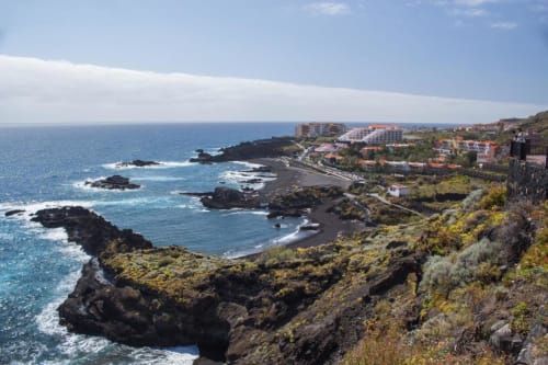 Acantilados costeros sobre playa de arena negra y aguas turquesas en La Palma, Islas Canarias con edificios hoteleros en el acantilado