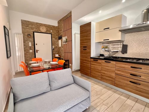 Moderno appartamento a Loano con open space, zona living e pranzo con sedie arancioni, cucina attrezzata e divano grigio