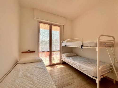Camera luminosa con letti a castello, letto singolo e porte sul balcone con vista sul giardino - Welcome Holiday a Loano, Italia