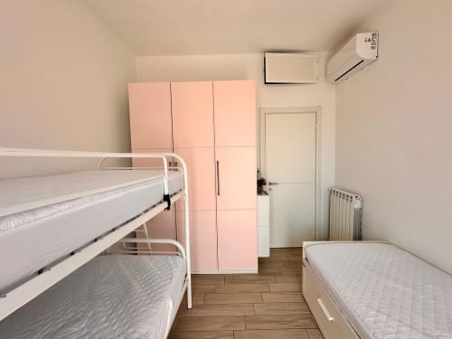Camera da letto luminosa con letti a castello, armadio rosa, pavimento in legno, climatizzatore e radiatore all'Oasi del mar presso Loano